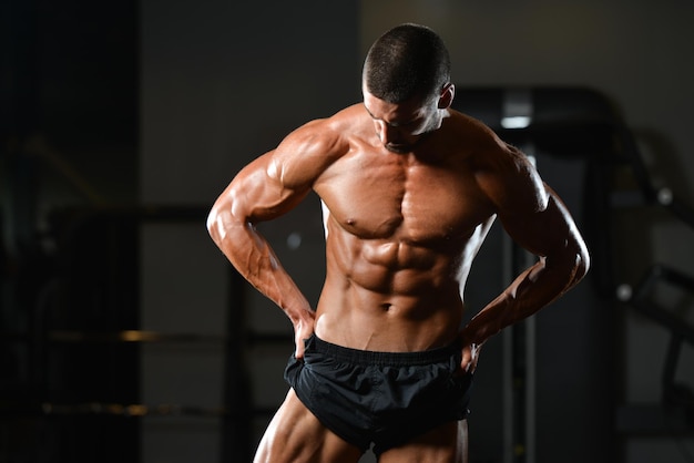 Uomo sano in piedi forte in palestra e flettendo i muscoli Modello di fitness bodybuilder atletico muscolare in posa dopo gli esercizi