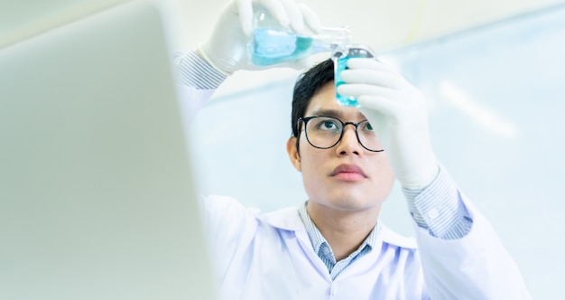 uomo scienziato che tiene la boccetta della provetta e che mescola la soluzione liquida scientifica al becher alla stanza del laboratorio