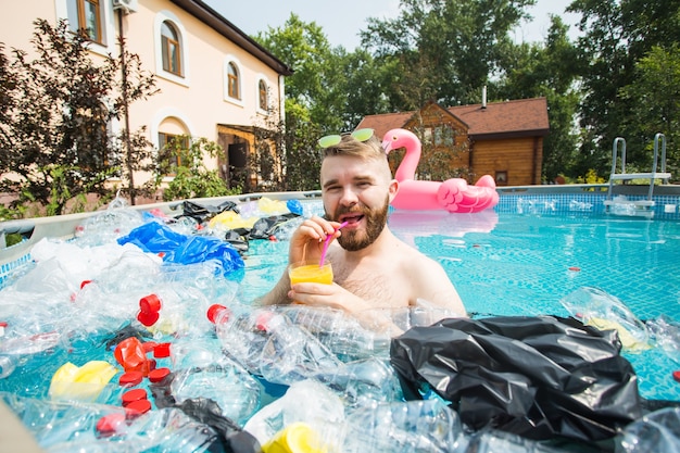 uomo sciocco nuotare e divertirsi in una piscina inquinata. Bottiglie e sacchetti di plastica galleggiano vicino a loro.