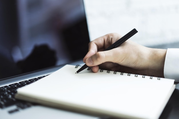 Uomo scrive con una penna in un quaderno su una tastiera portatile in un ufficio soleggiato business e concetto di istruzione Close Up