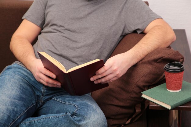 Uomo sdraiato sul divano e libro di lettura a casa