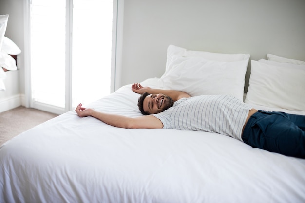 Uomo sdraiato sul letto con le braccia in alto sul letto in camera da letto