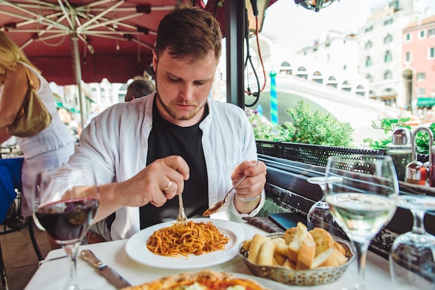 Uomo seduto al bar a mangiare pasta a bere vino ponte di rialto sullo sfondo venezia italia