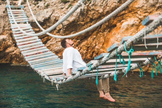 Uomo seduto al ponte sospeso che gode della vista sul mare e della calma della natura