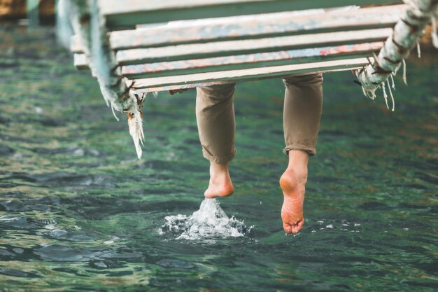 uomo seduto al ponte sospeso mettere le gambe in acqua di mare estate