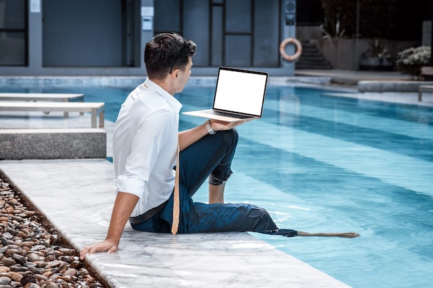 Uomo seduto davanti a un computer portatile vicino a una piscina