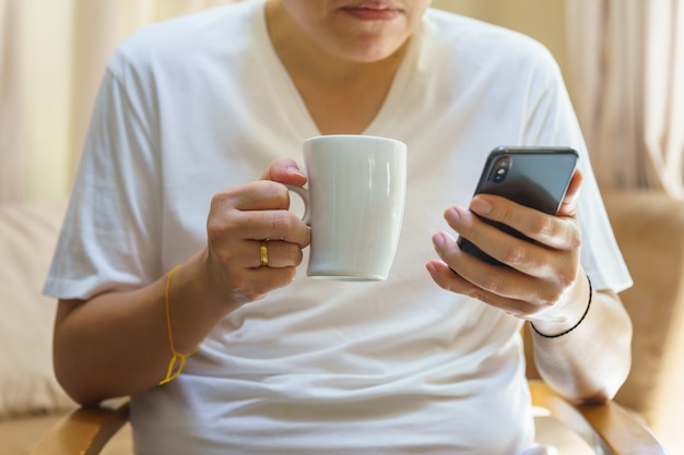 Uomo seduto e con in mano una tazza di caffè caldo e che utilizza lo smartphone mobile per la lettura