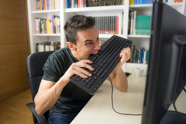 Uomo seduto in camicia nera davanti al computer, isterico perché non capisce qualcosa. Colpo a metà.