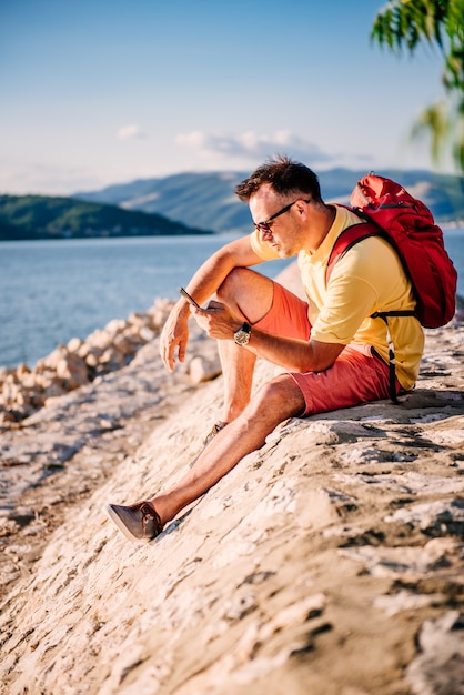 Uomo seduto in riva al mare e utilizzando smart phone