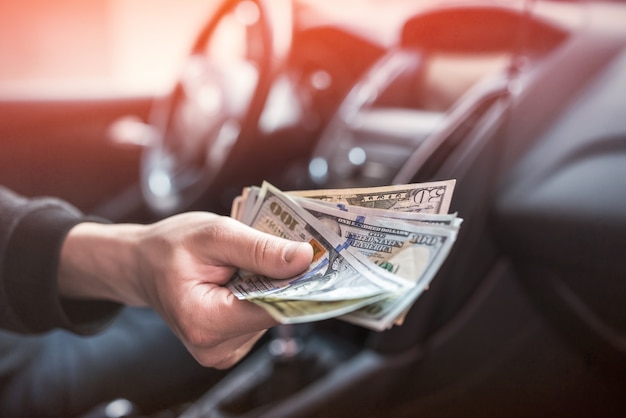 Uomo seduto in un'auto che conta banconote in dollari per o come tangenti, assicurazione o credito, investimenti. vendita o noleggio auto