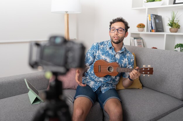 Uomo seduto in un salotto che insegna a suonare l'ukulele mentre registra un video con una videocamera