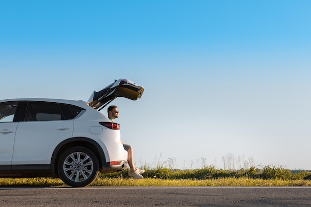 Uomo seduto nel bagagliaio dell'auto che si gode la vista dello spazio della copia del tramonto