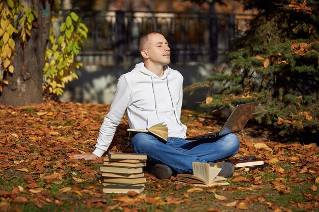 Uomo seduto nel parco con il computer portatile Blocchetto per appunti libri e libri di testo Apprendimento all'aperto allontanamento sociale