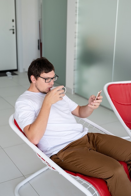 Uomo seduto su una sedia che guarda la tv con in mano una tazza di tè e un telefono