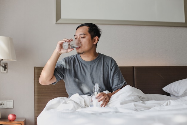 Uomo seduto sul letto e bevendo un bicchiere di acqua minerale dopo essersi svegliato dal sonno