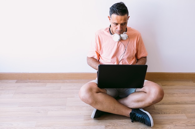 Uomo seduto sul pavimento con il suo laptop telelavoro da casa