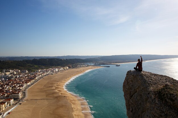 Uomo seduto sulla scogliera guardando dall'alto sulla spiaggia del mare e piccola città