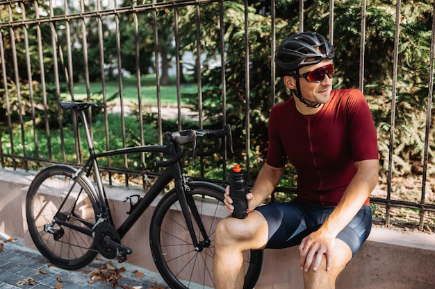 Uomo seduto vicino alla bici e con in mano una bottiglia d'acqua