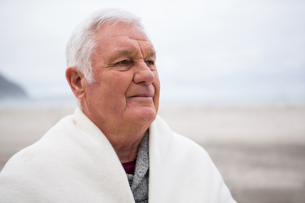 Uomo senior avvolto in scialle sulla spiaggia