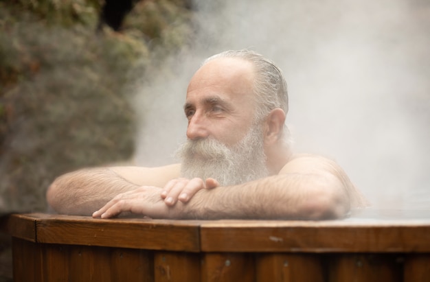 Uomo senior barbuto che gode del bagno termale nel centro di talassoterapia.