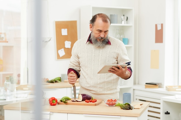 Uomo senior che cucina le verdure in cucina