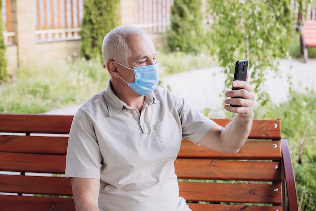 Uomo senior che indossa maschera medica con lo smartphone. concetto di coronavirus. protezione respiratoria