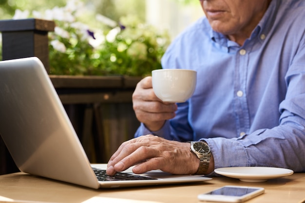Uomo senior che per mezzo del computer portatile durante la pausa caffè