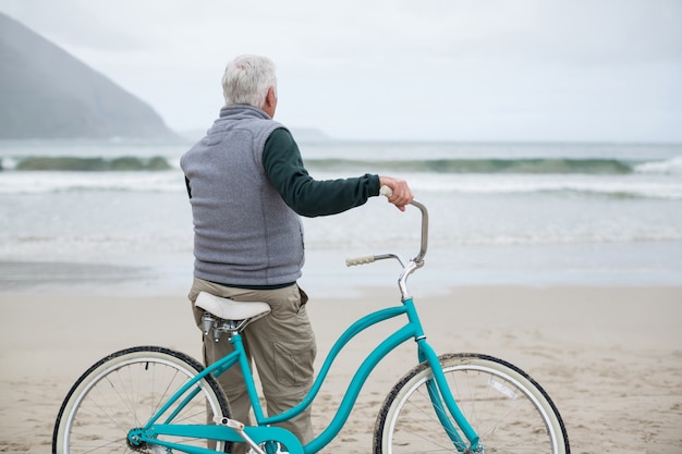 Uomo senior che sta con la bicicletta sulla spiaggia