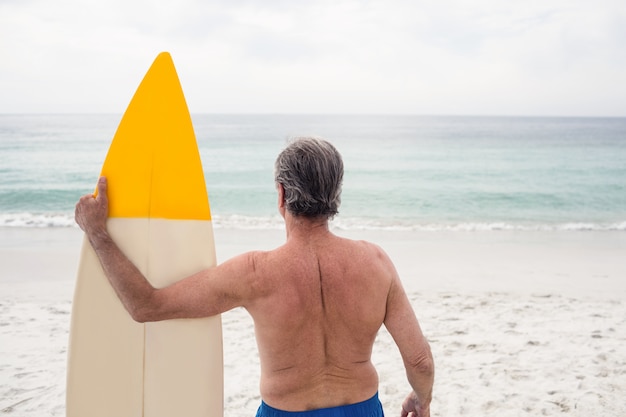 Uomo senior che sta sulla spiaggia con il surf