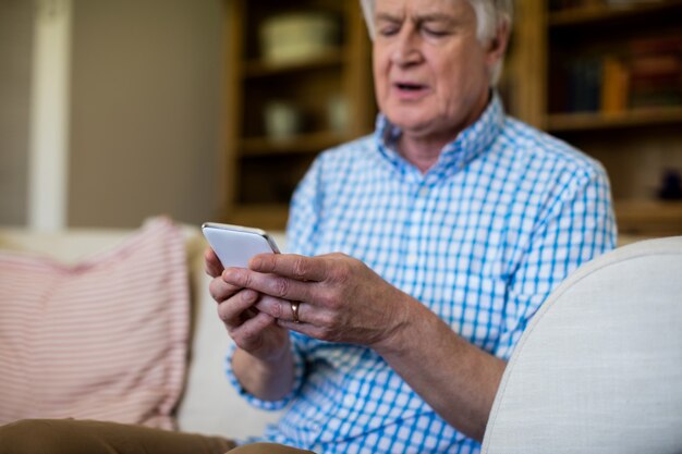 Uomo senior che utilizza telefono cellulare nel salone