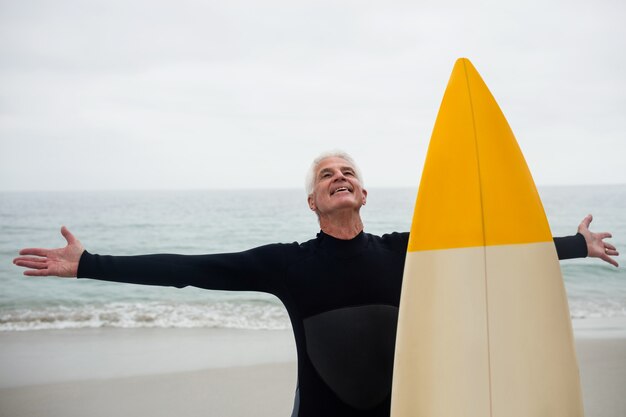 Uomo senior felice con il surf che sta sulla spiaggia