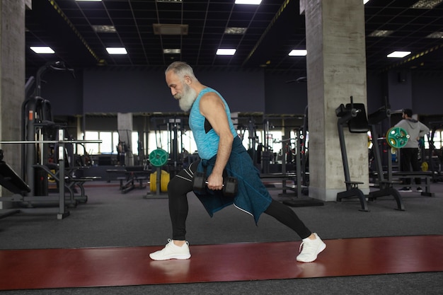 Uomo senior in abbigliamento sportivo in palestra che risolve con i pesi.