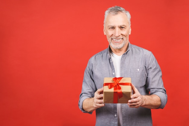 Uomo senior maturo che mostra un regalo con il nastro rosso come presente isolato.