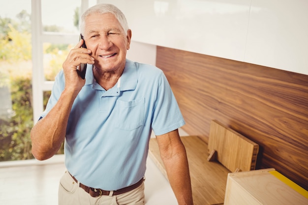 Uomo senior sorridente su una telefonata in salone