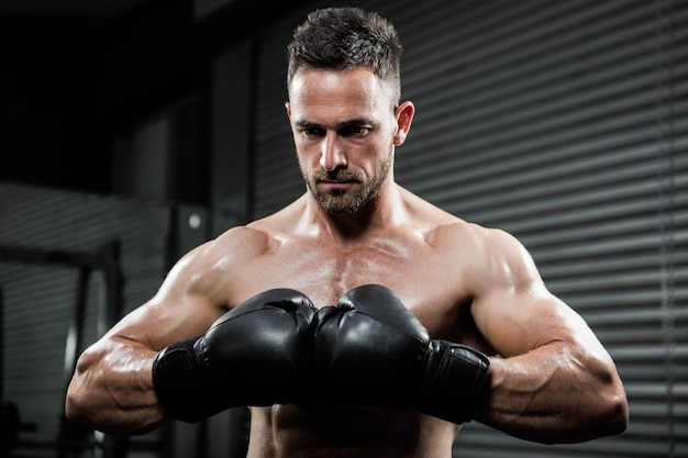 Uomo senza camicia arrabbiato con i guanti della scatola nella palestra di CrossFit