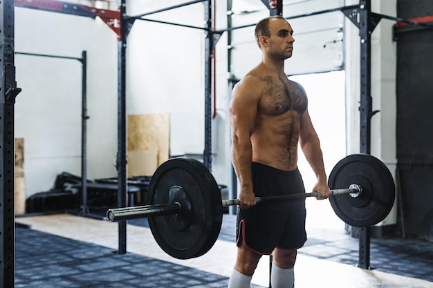 Uomo senza camicia che fa sollevamento morto in palestra