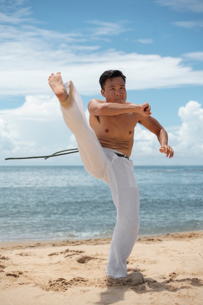 Uomo senza camicia che pratica capoeira sulla spiaggia