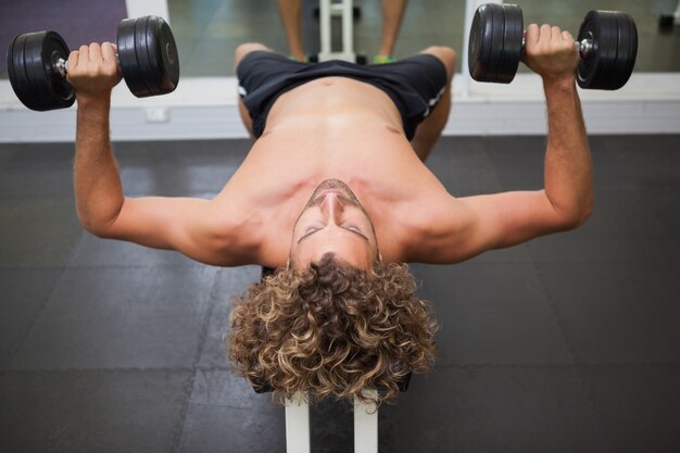 Uomo senza camicia che si esercita con i dumbbells in ginnastica