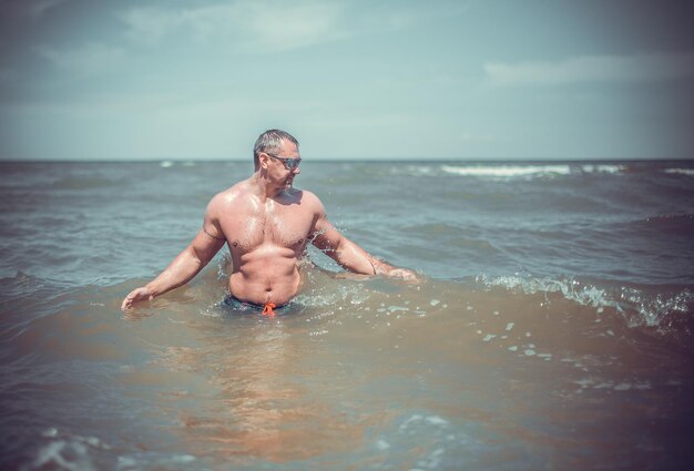 Uomo senza camicia in piedi in mare