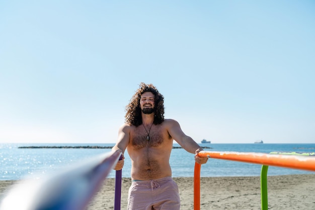 Uomo senza camicia riccio felice che si esercita sulla spiaggia