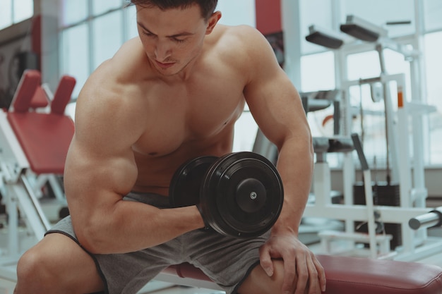 Uomo senza camicia strappato che si esercita con le teste di legno alla palestra