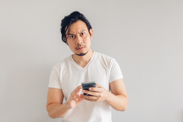 Uomo serio capelli lunghi in maglietta casual bianca sta utilizzando smartphone.