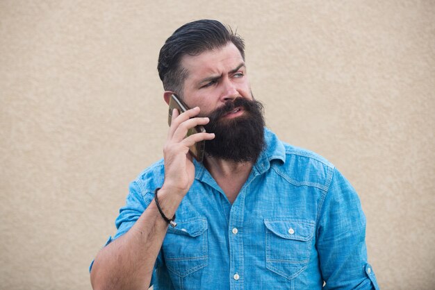 Uomo serio con la barba in piedi all'aperto utilizzando il telefono cellulare.