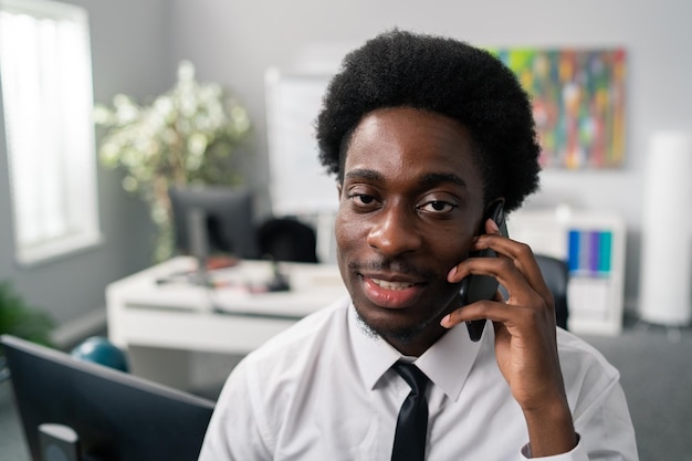 Uomo serio concentrato con un afro sulla testa che indossa una camicia e cravatta siede in ufficio a parlare per affari