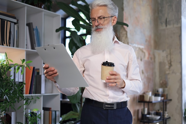 Uomo serio di affari maturi in camicia bianca che legge il contratto mentre si trova in ufficio.