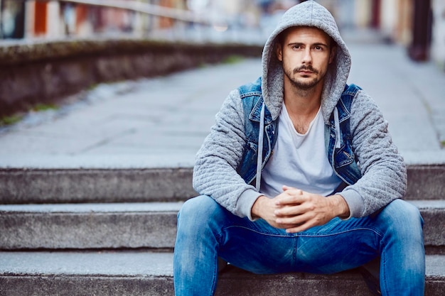 Uomo serio in giacca con cappuccio seduto sulle scale