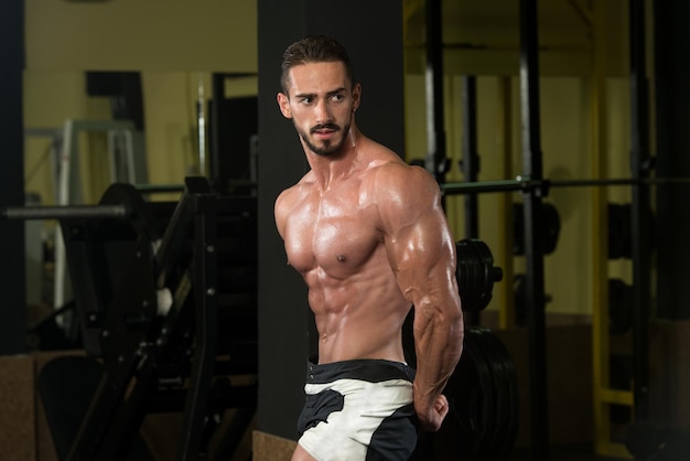 Uomo serio in piedi forte in palestra e flettendo i muscoli