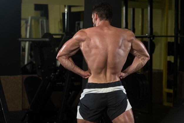 Uomo serio in piedi forte in palestra e flettendo i muscoli