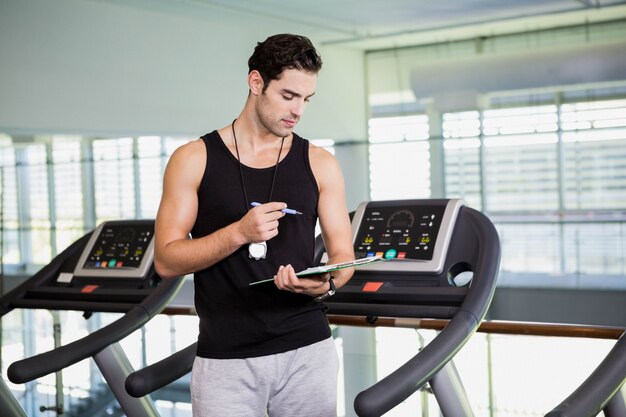 Uomo serio sul tapis roulant che esamina appunti in palestra