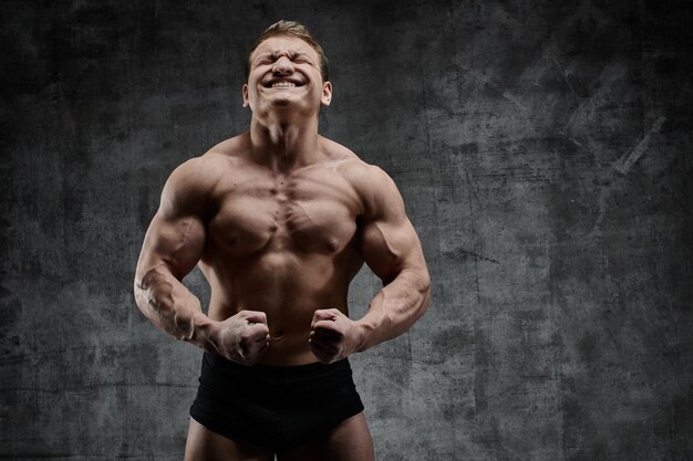 Uomo sexy bodybuilder in posa su sfondo scuro in pantaloncini neri. Bel corpo maschile pompato isolato con spazio libero per la pubblicità